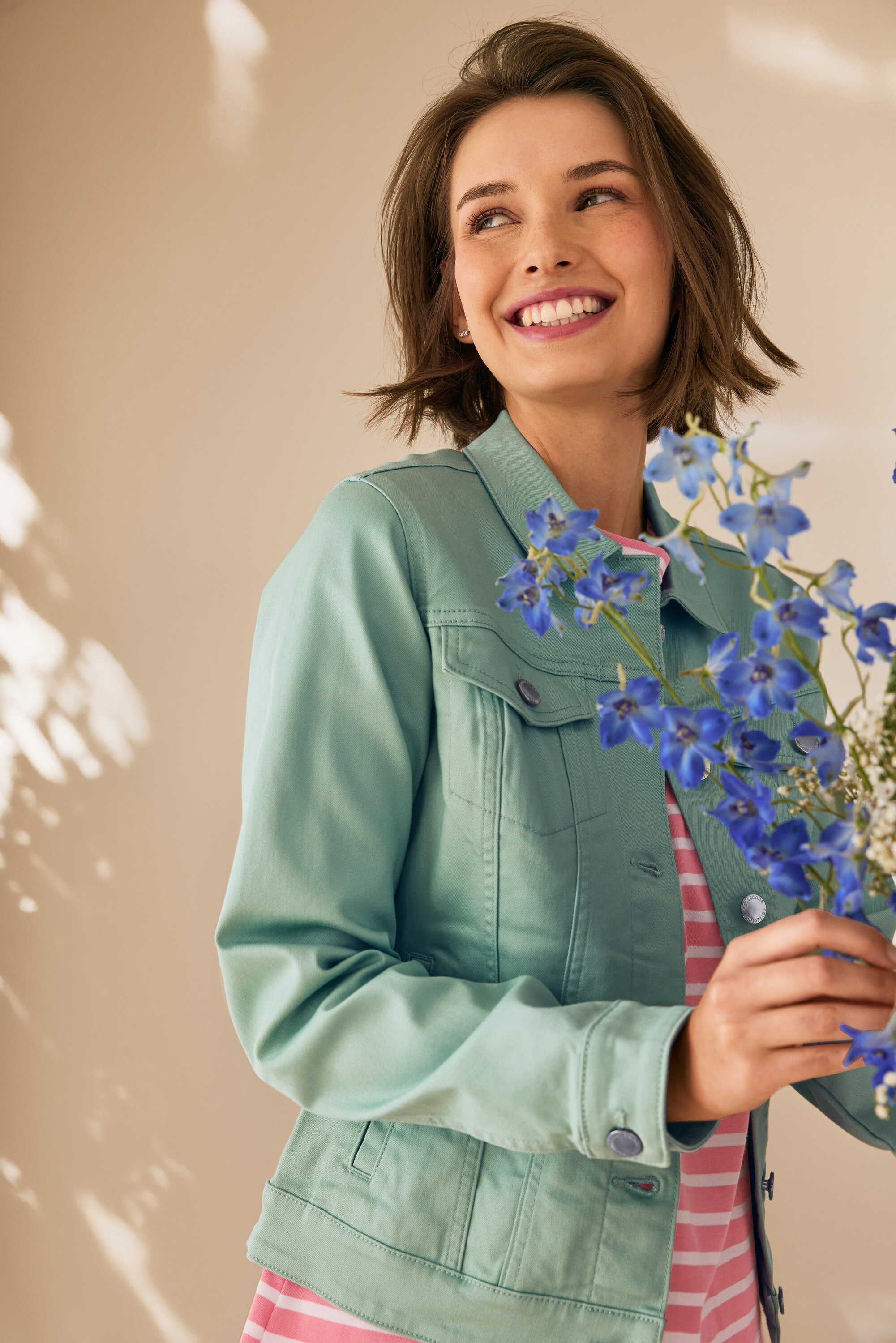 Femme souriante tenant des fleurs bleues, portant une veste en jean vert menthe et des puces d’oreille avec arc en zircons en argent 925.