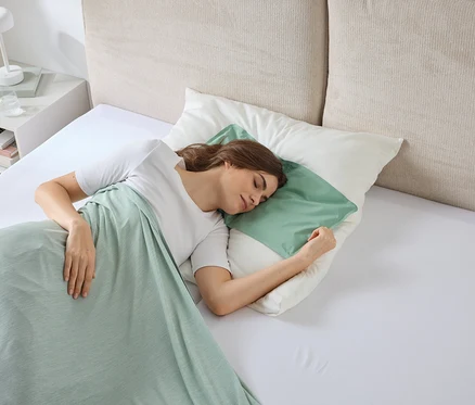Femme dormant dans un lit sous une couverture vert clair, la tête sur un oreiller avec une taie d'oreiller vert menthe.