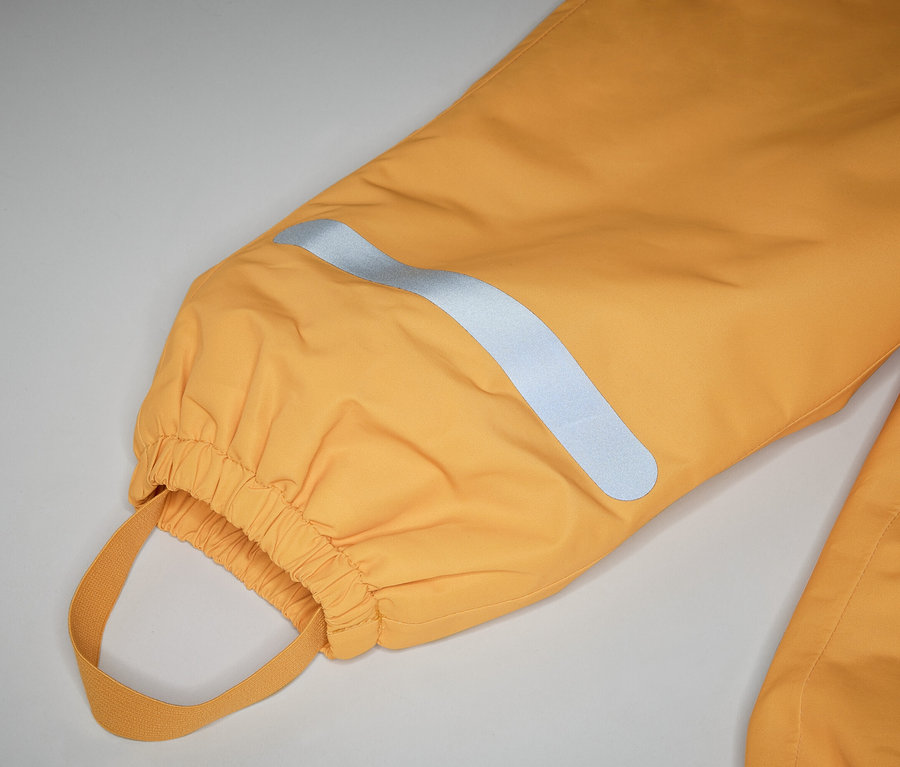 Gros plan sur une jambe de pantalon jaune avec élastique, boucle et bande réfléchissante sur fond clair.