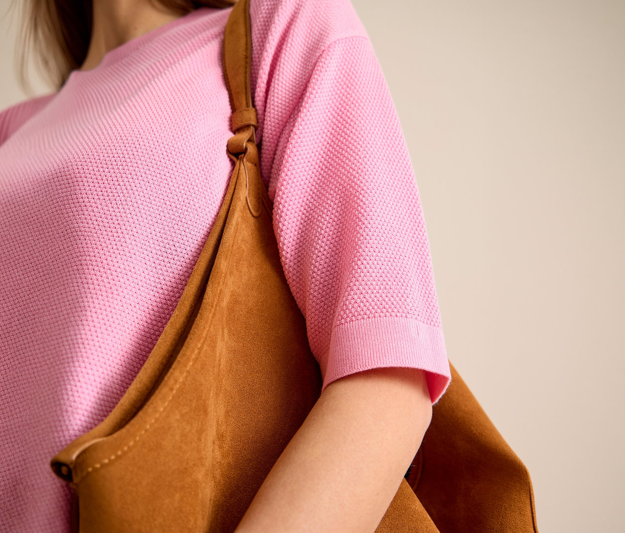 Une femme porte un pull à manches courtes rose CECIL et un sac marron à l'épaule.