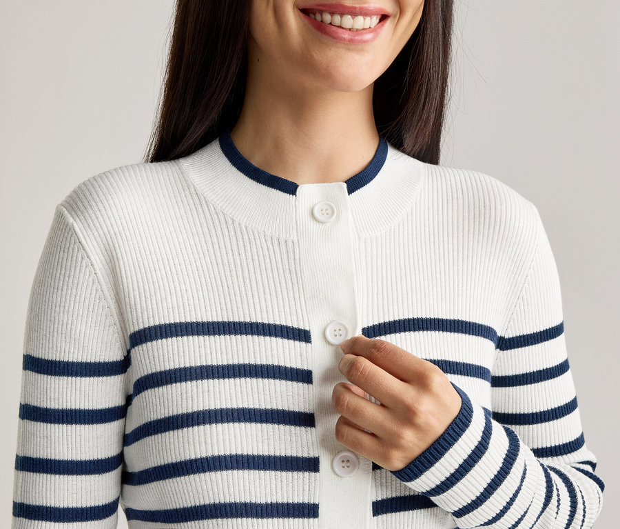 Une femme boutonne un cardigan rayé blanc et bleu marine.