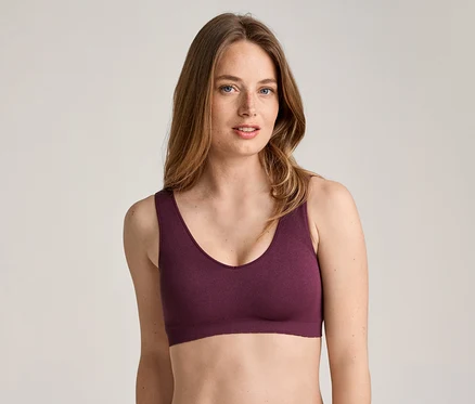 Une femme aux longs cheveux ondulés châtain clair et aux taches de rousseur, portant un soutien-gorge de sport bordeaux.