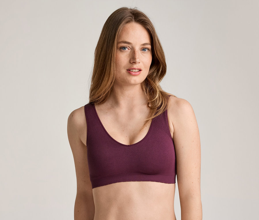 Une femme aux longs cheveux ondulés châtain clair et aux taches de rousseur, portant un soutien-gorge de sport bordeaux.