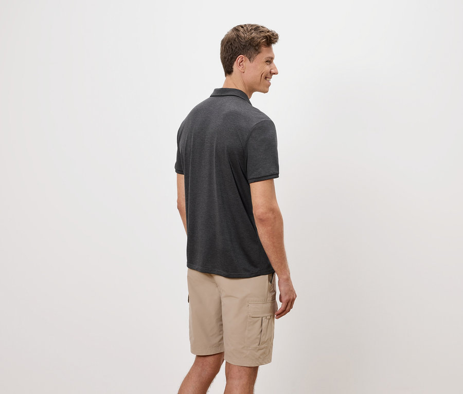 Un homme se tient de côté, portant un polo gris et un short cargo beige sur un fond blanc.