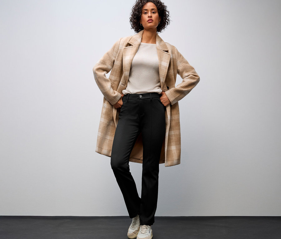 Femme portant un manteau beige et un pantalon bootcut Street One, les mains sur les hanches.