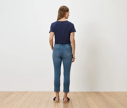 Vue arrière d'une femme portant un t-shirt bleu et un jean devant un mur blanc.