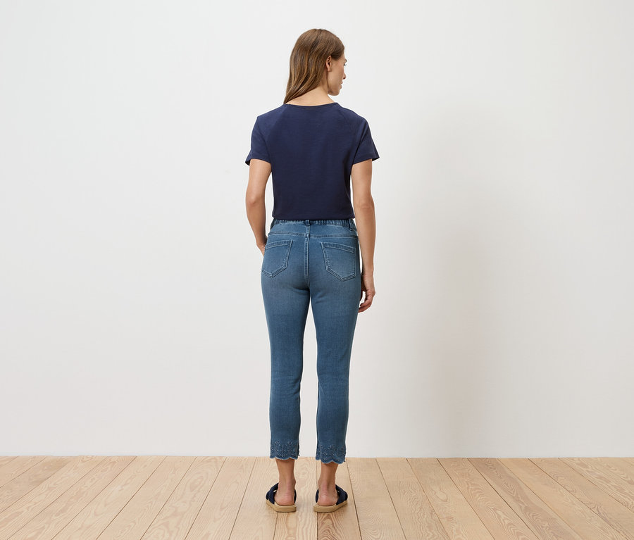 Vue arrière d'une femme portant un t-shirt bleu et un jean devant un mur blanc.