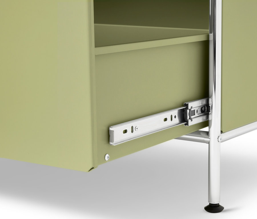Gros plan d'une armoire vert clair avec des pieds argentés et un tiroir partiellement ouvert.