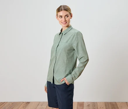 Une femme aux cheveux blonds porte une chemise vert clair et un short.