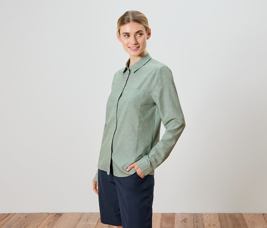 Une femme aux cheveux blonds porte une chemise vert clair et un short.