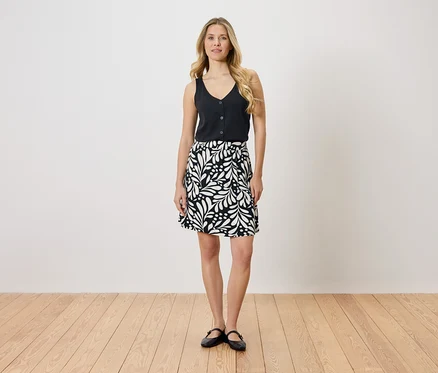 Femme blonde portant un haut noir et une jupe noire et blanche à motifs de feuilles.