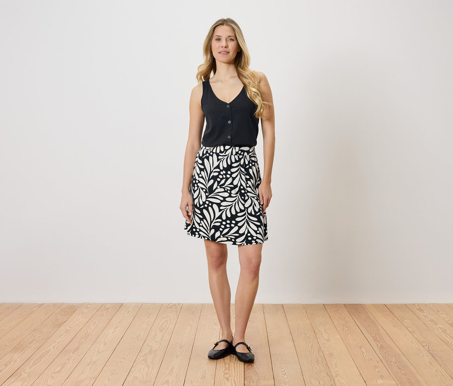 Femme blonde portant un haut noir et une jupe noire et blanche à motifs de feuilles.