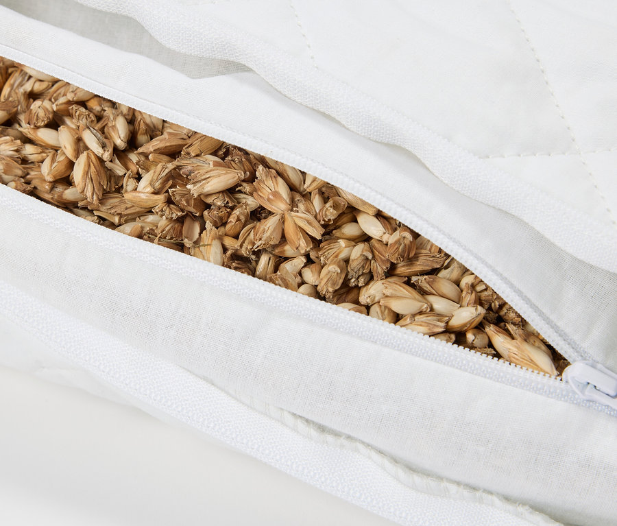 Gros plan d'un oreiller blanc partiellement ouvert rempli de céréales.