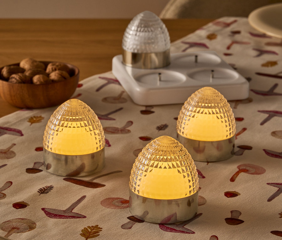 Trois bougeoirs chauffe-plat en forme de ruche ambrée allumés et un bougeoir chauffe-plat transparent sur un chemin de table à motifs de champignons.