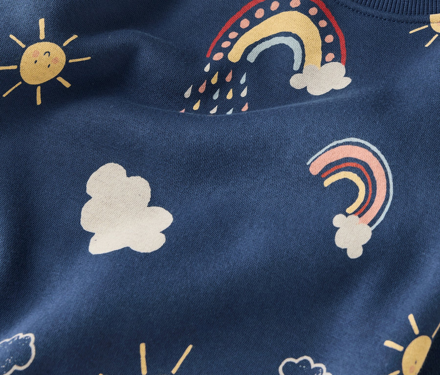 Gros plan d'un tissu bleu marine avec des motifs répétés de soleils jaunes, de nuages blancs et d'arcs-en-ciel colorés.