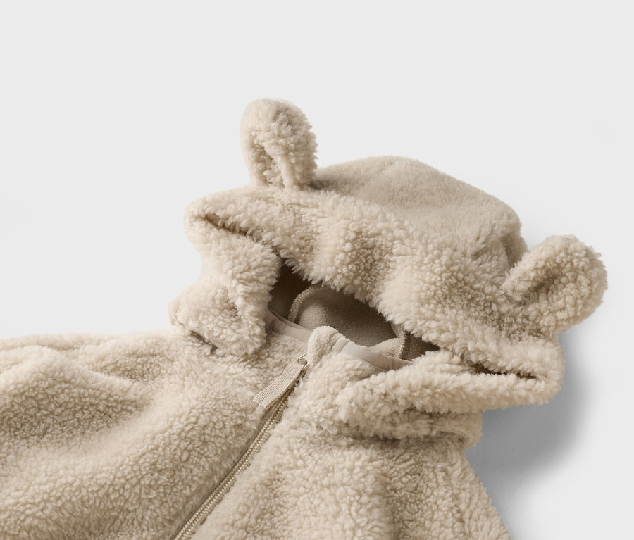 Gros plan d'une veste beige duveteuse à capuche avec des oreilles sur fond blanc.