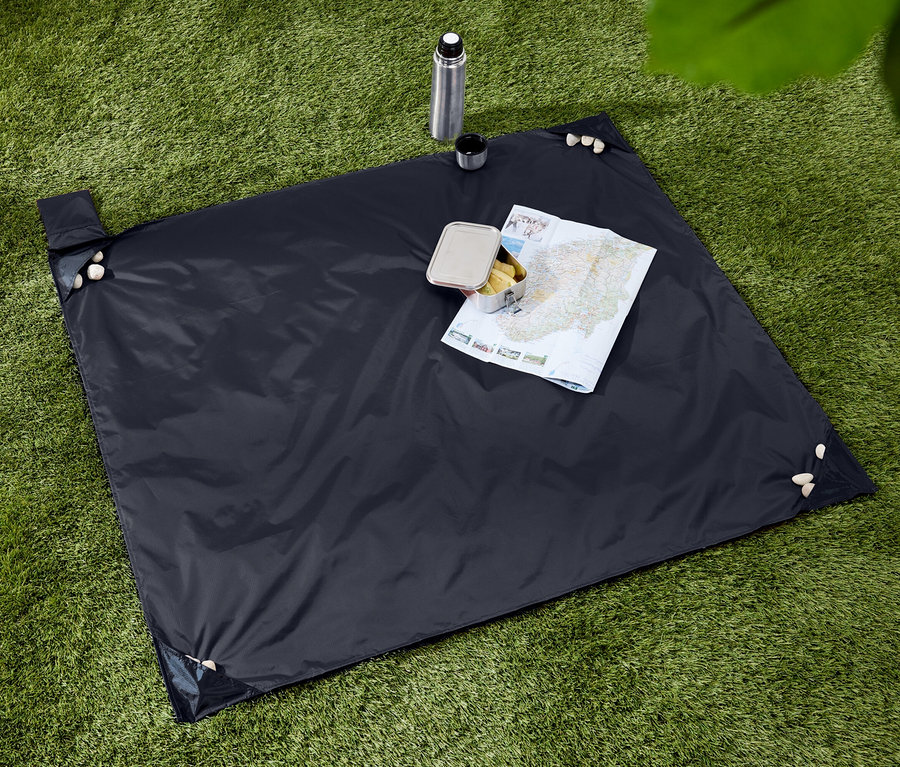 Couverture de pique-nique bleu foncé avec des collations, une thermos et une carte sur une pelouse verte.