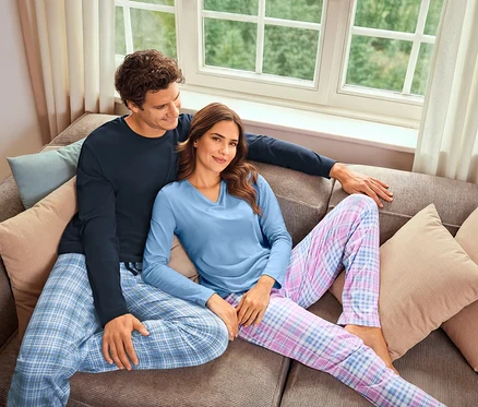 Un homme et une femme sont assis sur un canapé. L'homme porte un pyjama bleu marine et la femme un pyjama bleu clair à carreaux.