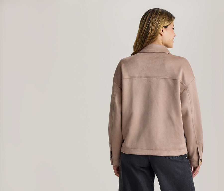 Femme vue de dos, portant une veste à col marron clair effet daim et un pantalon foncé, regardant vers sa droite.