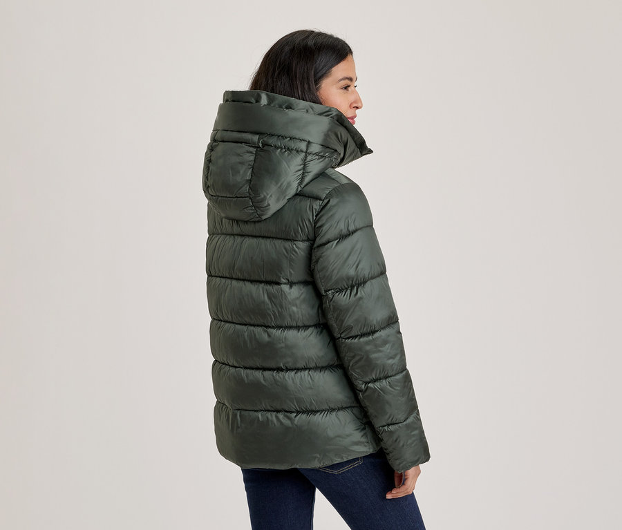 Femme vue de profil, portant une doudoune vert foncé à capuche et un jean bleu foncé, regardant vers la droite.