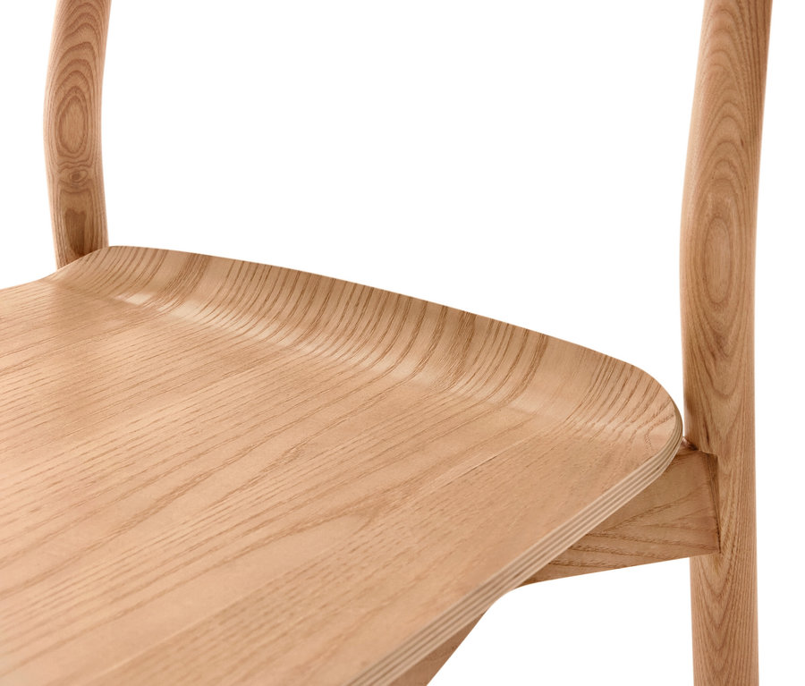 Gros plan d'une chaise en bois clair, montrant l'assise incurvée avec le grain du bois visible et des parties des montants incurvés du dossier.