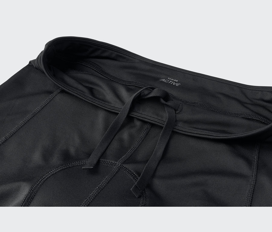 Vêtement de sport noir avec cordon de serrage à la taille et coutures apparentes. Une étiquette indique "TCHIBO ACTIVE".
