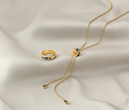 Sur un tissu blanc reposent une chaîne dorée «Iconic» et une bague dorée «Iconic».