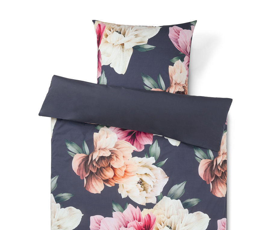 Parure de lit florale sur fond bleu foncé avec de grandes fleurs roses, crème et pêche. Un oreiller uni bleu foncé est posé dessus.