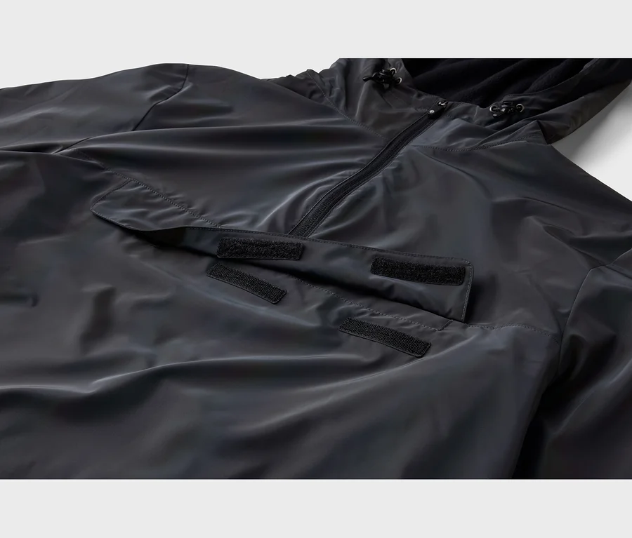 Gros plan d'une veste anorak noire avec une demi-fermeture éclair, une capuche à cordons de serrage et une grande poche à rabat avant avec fermetures auto-agrippantes.