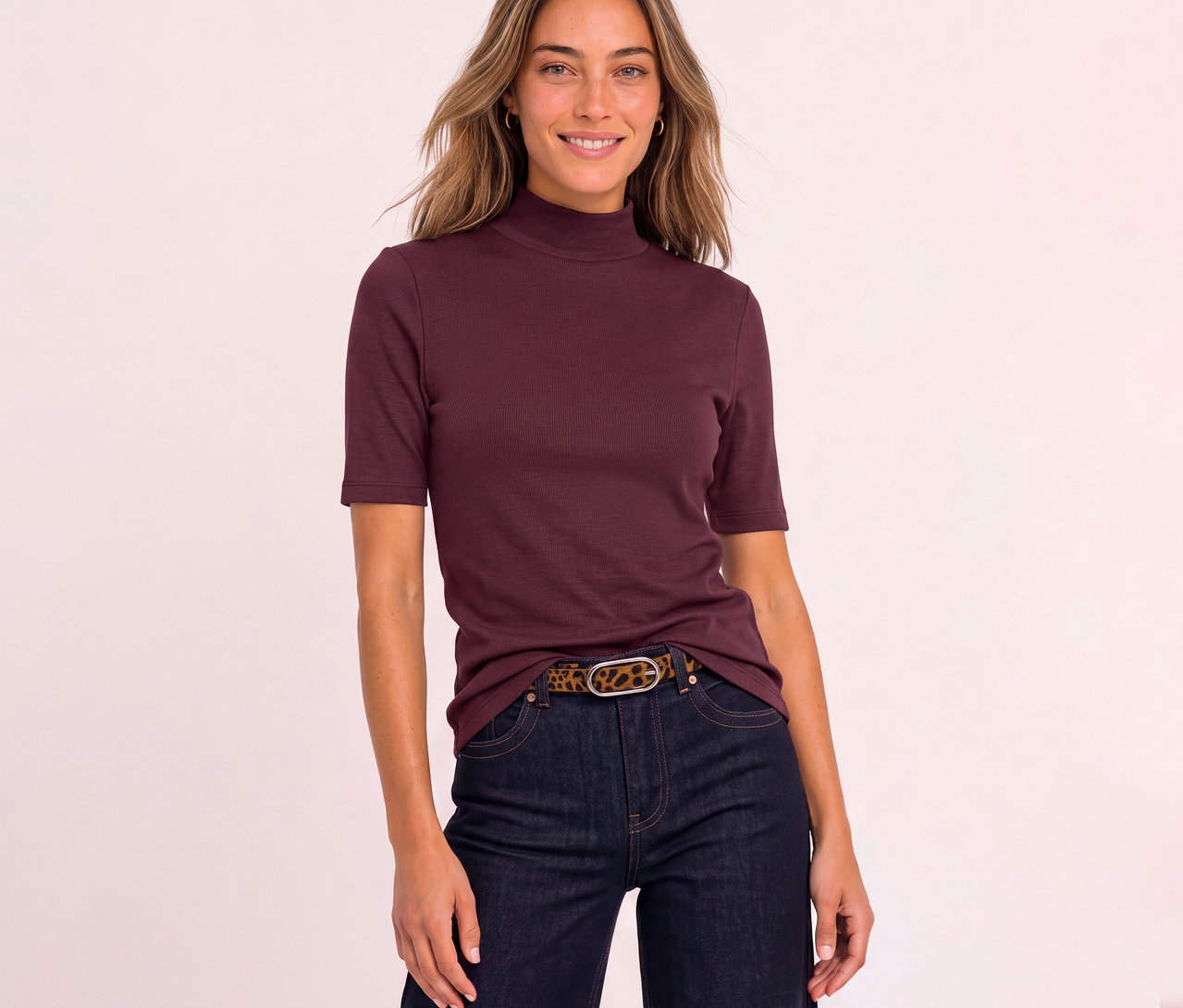Femme souriante portant un T-shirt Street One rouge côtelé à col montant et manches courtes, un jean foncé et une ceinture léopard.