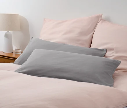 Deux taies d'oreiller en jersey gris sur un lit avec du linge de lit rose.