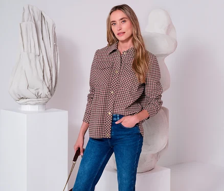 Une femme porte une veste Street One à carreaux marron et noir et un jean bleu, la main dans la poche, devant des sculptures abstraites.