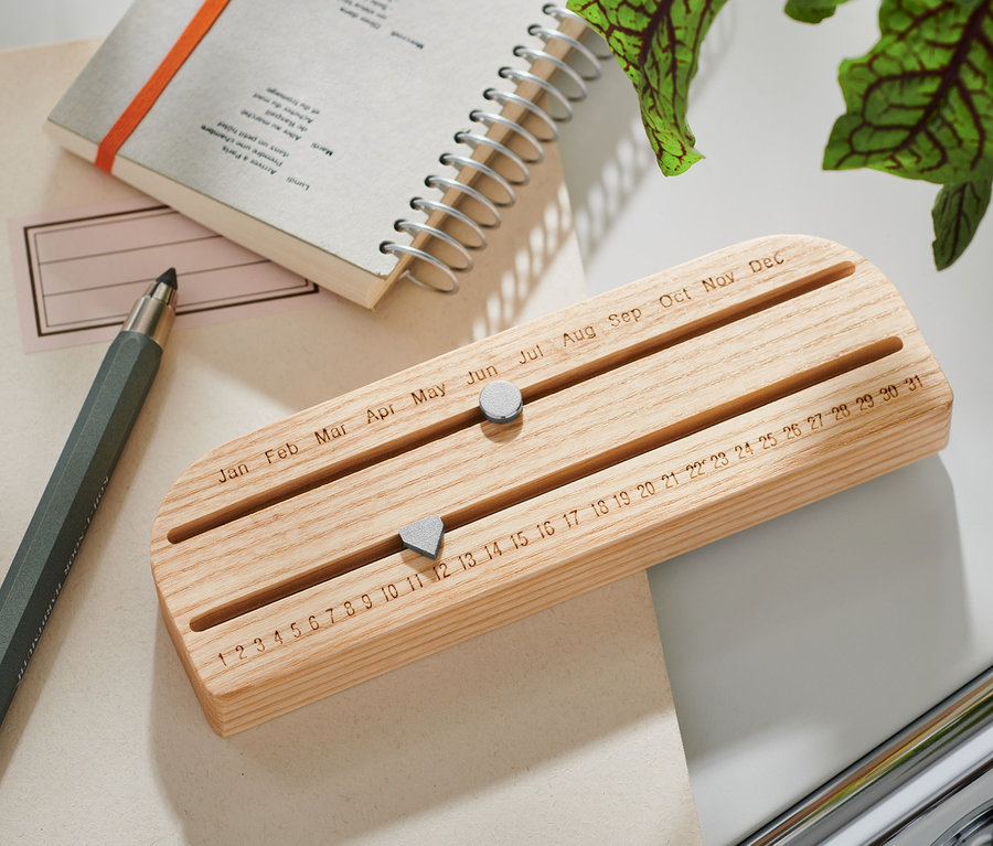 Un calendrier éternel en bois est posé sur une table à côté d'un bloc-notes et d'un stylo.