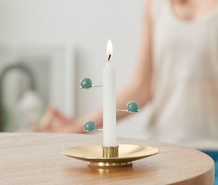 Une bougie de méditation allumée sur une table, avec une femme en arrière-plan en position de méditation.