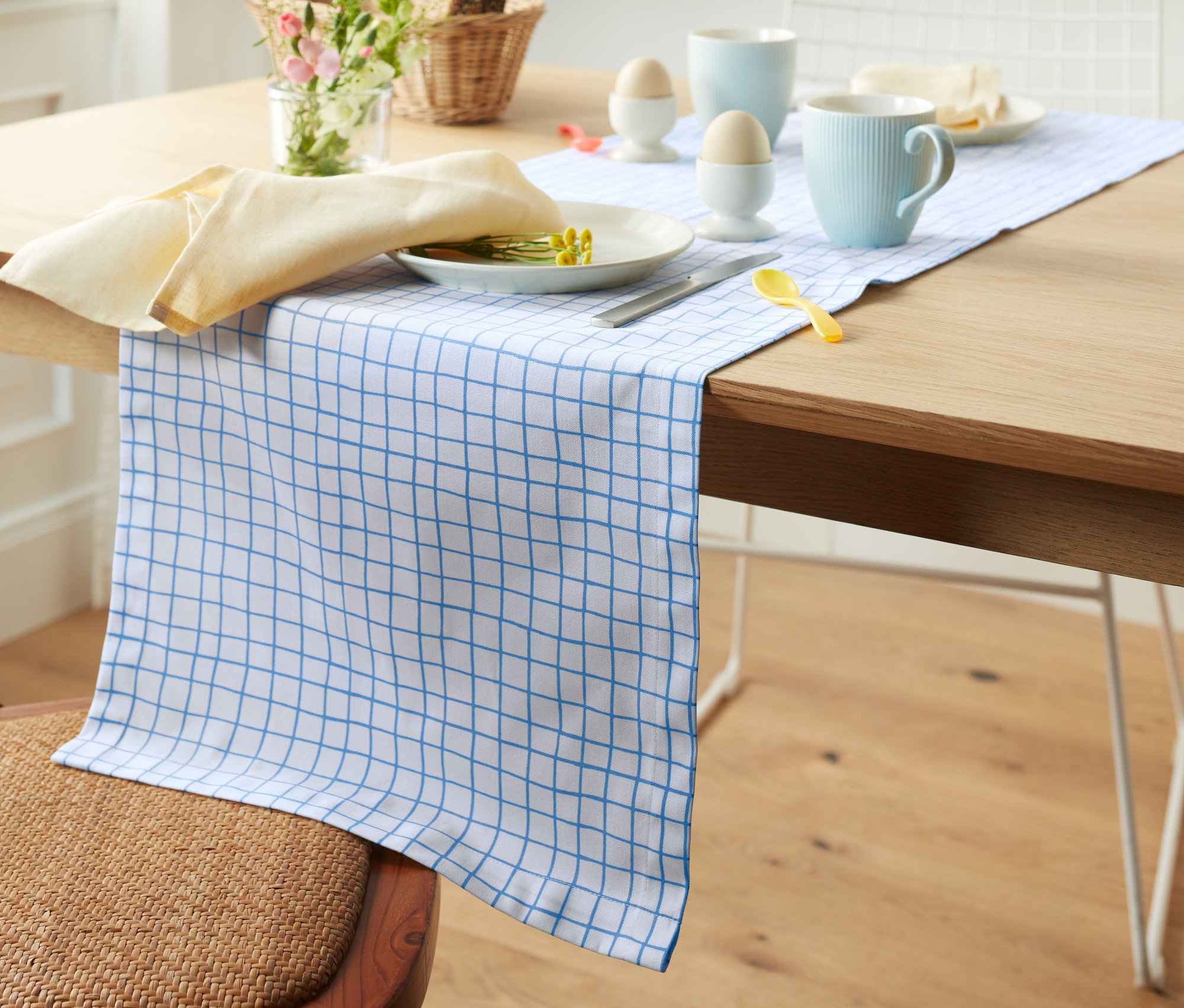 Table avec un chemin de table imprimé intégral, une assiette, une tasse et une serviette sont dressées.