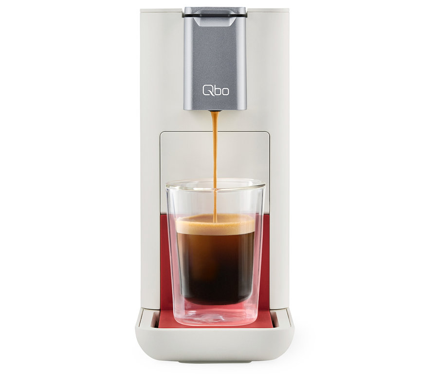 Le café coule d'une machine à café Qbo ESSENTIAL Bright Coral dans un verre.