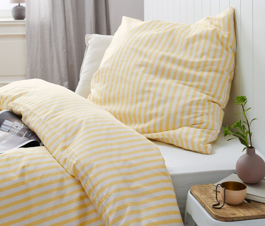 Linge de lit en renforcé rayé jaune et blanc de différentes tailles sur un lit.