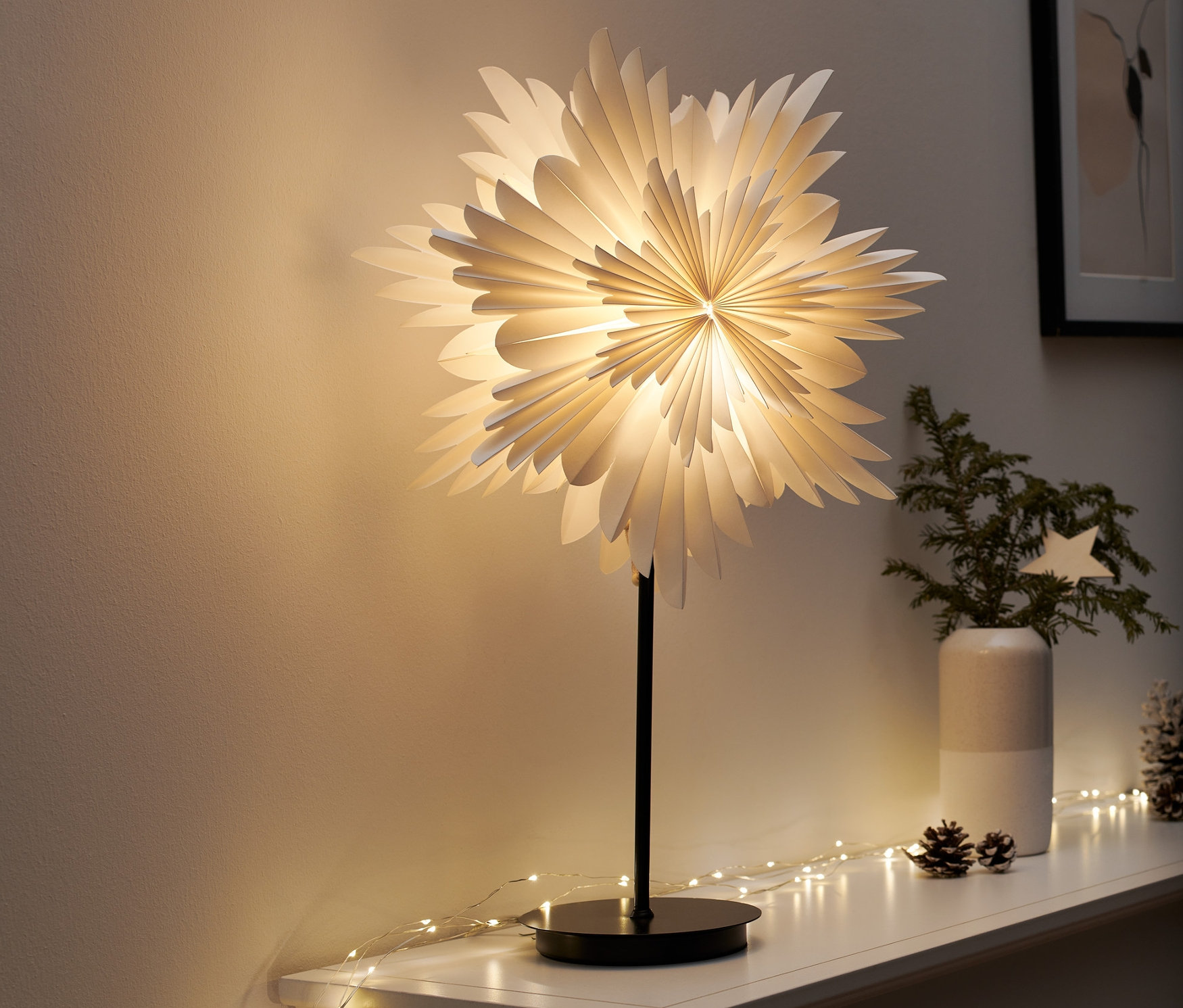 Un éclairage décoratif à LED « étoile » est posé sur une étagère blanche. Des guirlandes lumineuses et des décorations de Noël l'entourent.