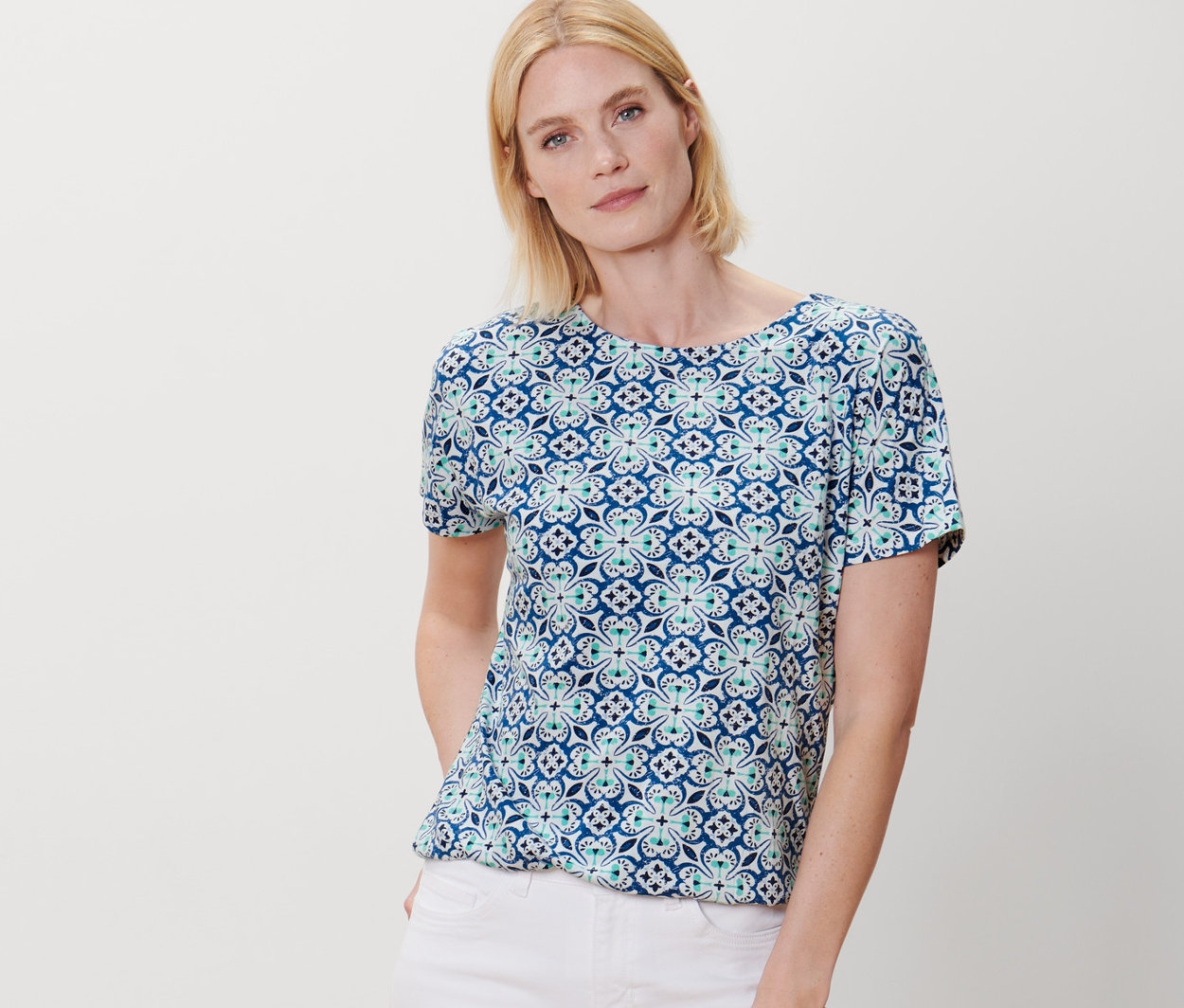 Femme posant en blouse avec imprimé intégral et pantalon blanc.