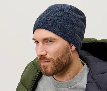Un homme porte un bonnet en maille bleu foncé chiné, un pull gris et une doudoune verte.