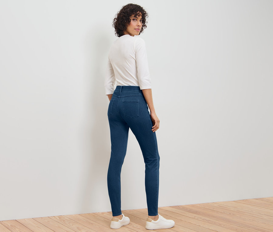 Une femme regarde par-dessus son épaule et porte un jegging, un t-shirt blanc et des baskets blanches.