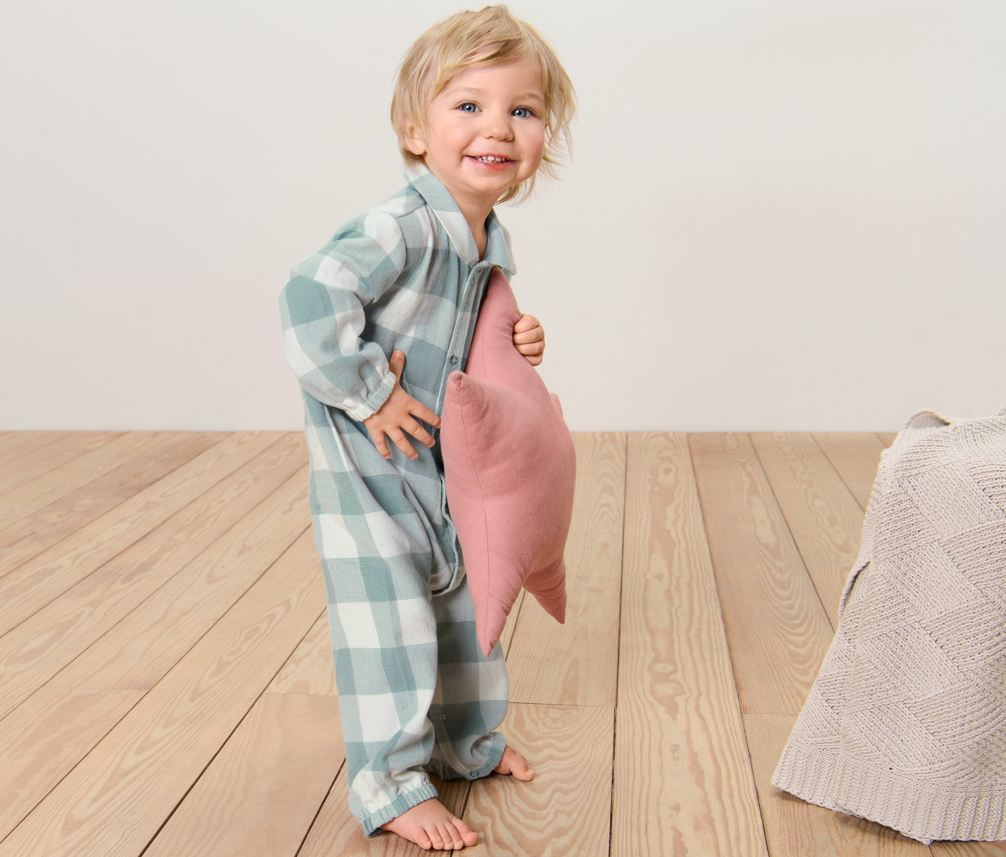 Un enfant souriant tient un oreiller rose dans un pyjama pour bébé en flanelle.