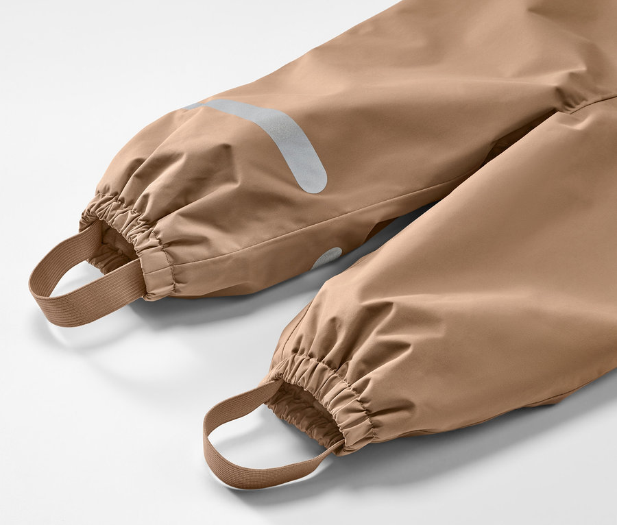 Détail d'un pantalon de pluie thermique pour enfant, marron, avec poignets élastiques et réflecteurs.