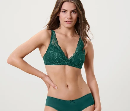 Une femme pose en soutien-gorge à coques souples en dentelle vert foncé et culotte assortie.