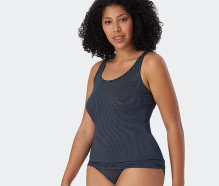 Femme aux cheveux bouclés portant un débardeur à bretelles SCHIESSER bleu foncé à rayures avec modal et une culotte assortie.