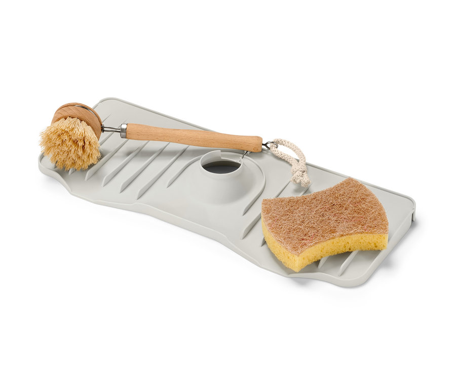 Une étagère en silicone pour robinet avec une brosse et une éponge sur un fond blanc.
