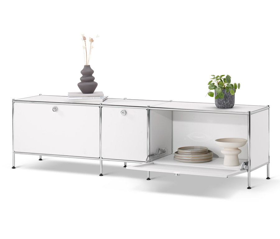 Meuble bas « CN3 » blanc avec 3 abattants. Un vase, un livre et une plante en pot sont posés sur le meuble bas.