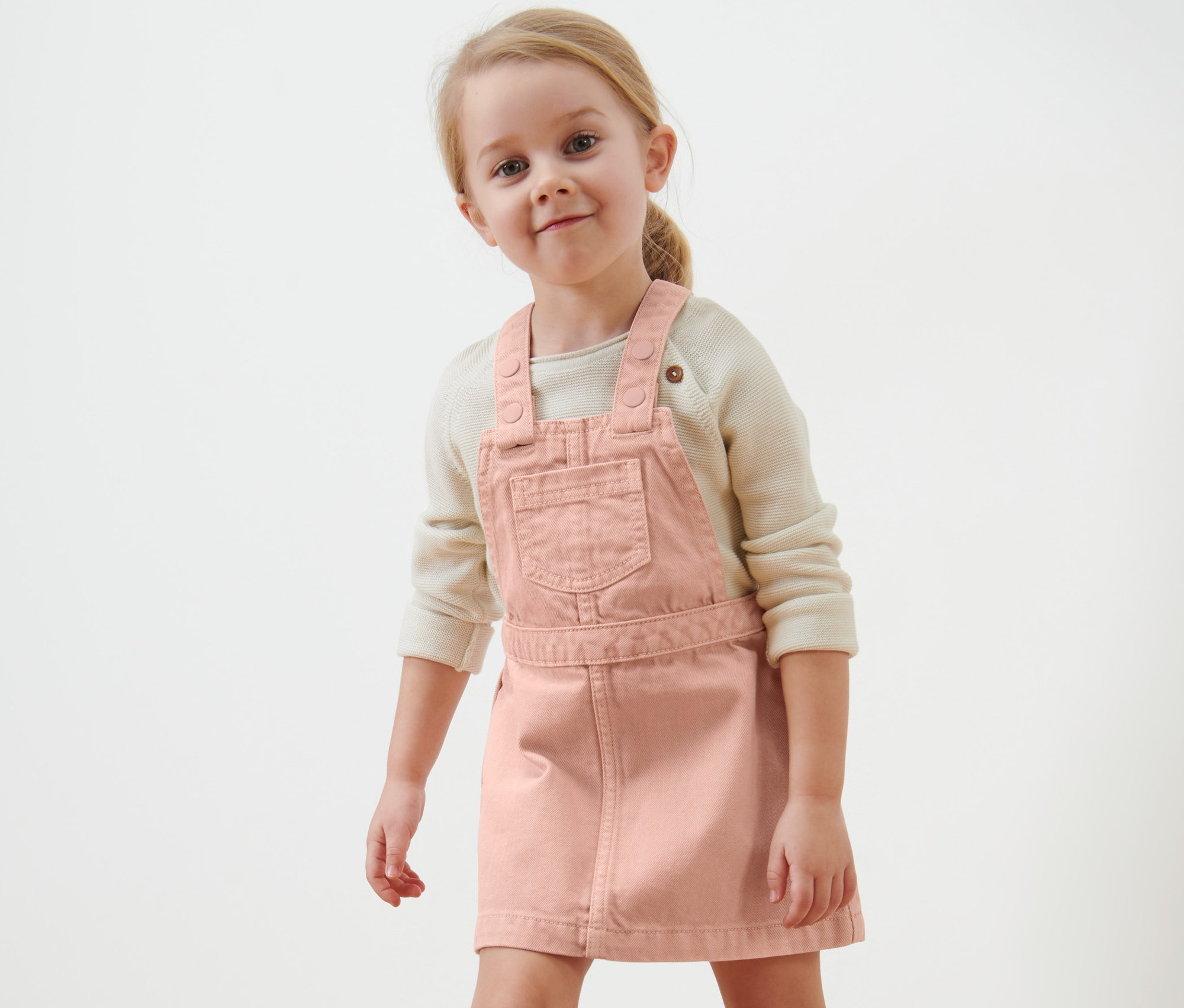 Fillette blonde souriante portant une robe-salopette pour enfant.