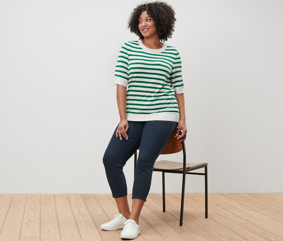 Une femme est assise sur une chaise et porte un pull en maille fine rayé et un jeggings 7/8.