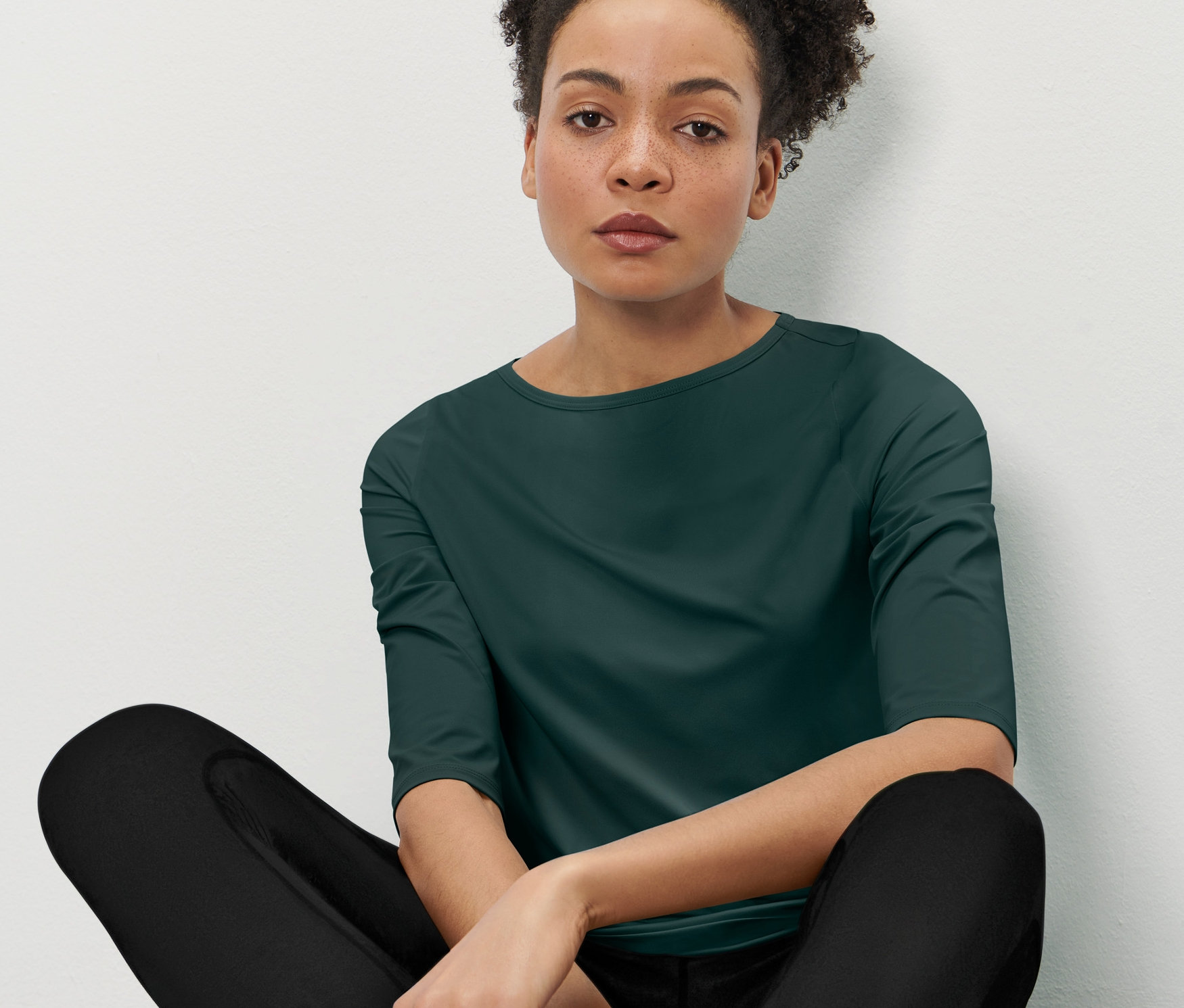 Femme assise portant un t-shirt technique manches 3/4 vert foncé.